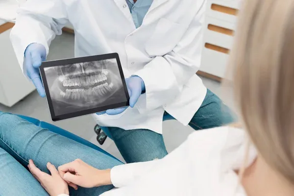 Dentista mostrandole a su paciente una radiografía tomada con herramientas que tienen implementada odontología digital actualizada